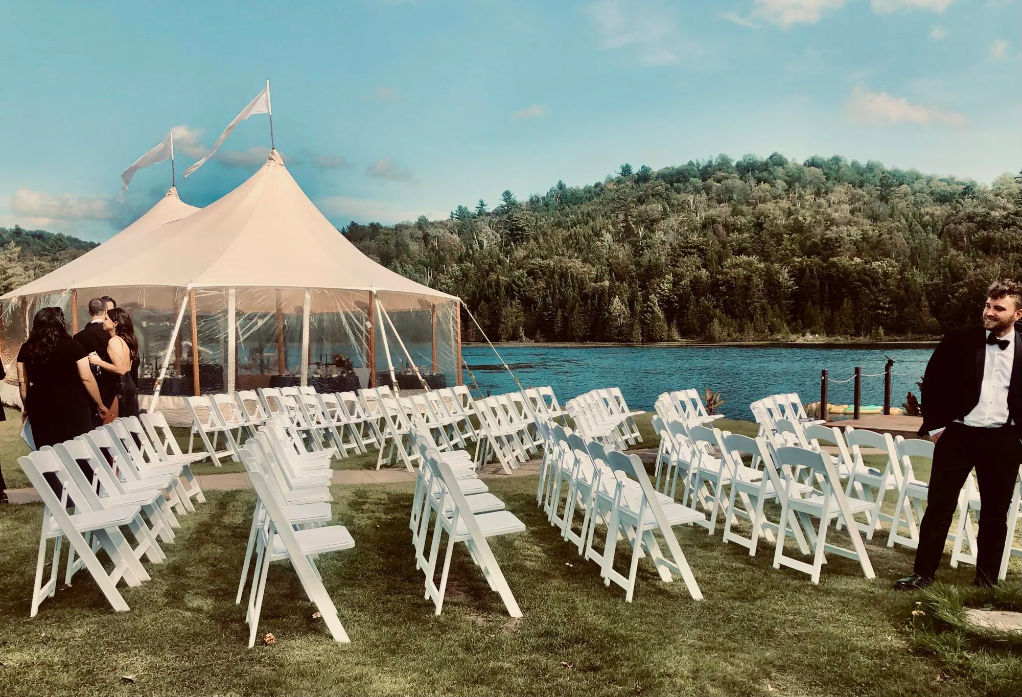 Chapiteau transparent et rangées de chaises blanches au bord du lac