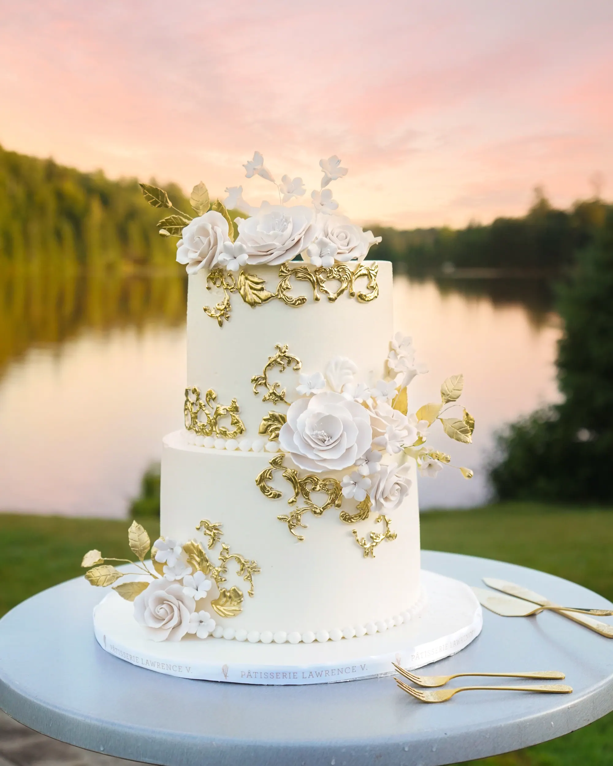Gâteau de mariage blanc et or devant le lac au coucher du soleil
