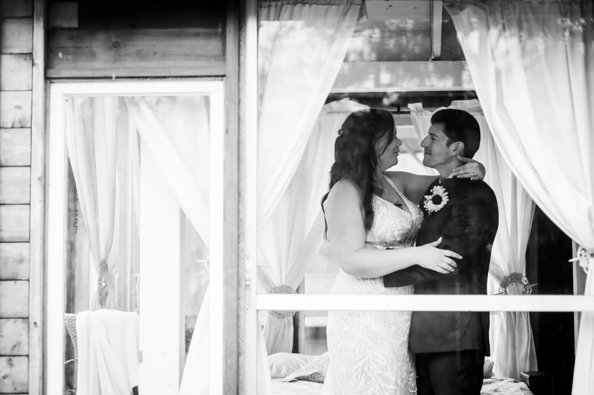 Les mariés enlacés dans le gazebo aux voilages blancs, noir et blanc