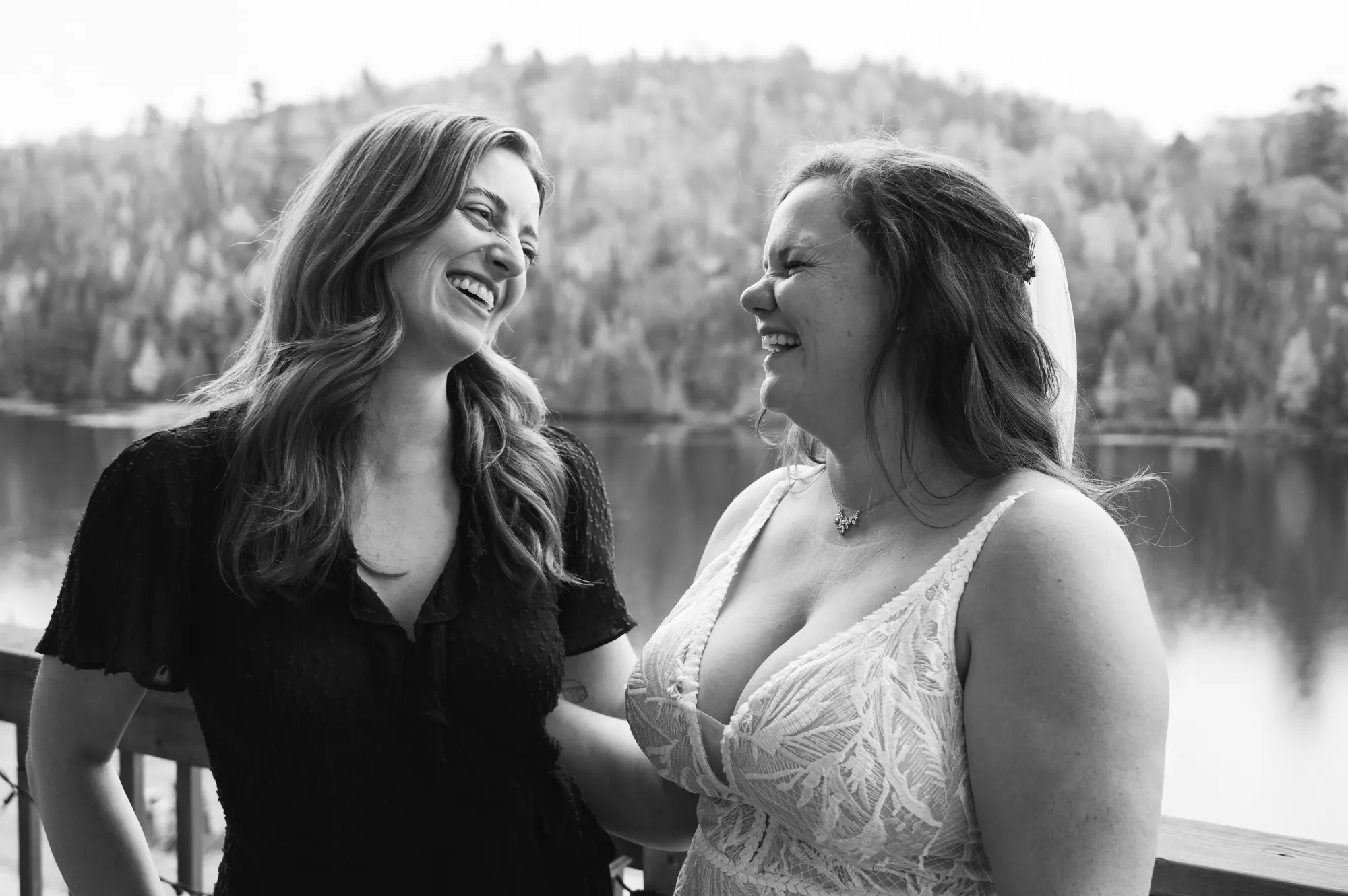 La mariée et sa témoin rient sur la terrasse face au lac, noir et blanc
