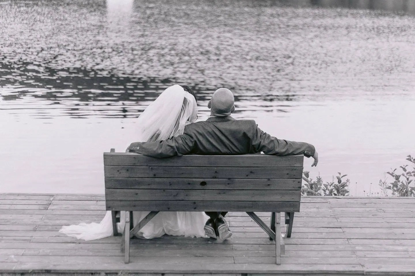 Les mariés assis sur un banc face au lac, noir et blanc