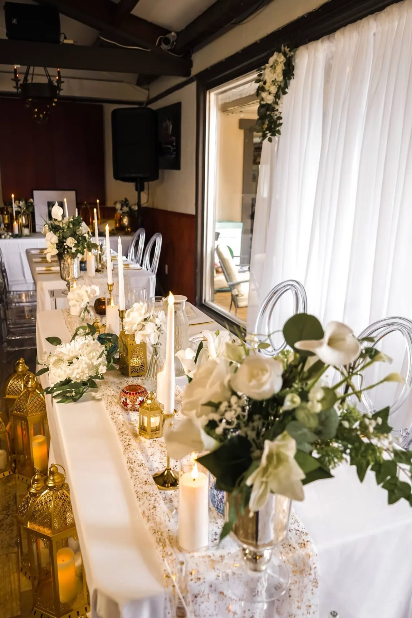 Table d'honneur : lanternes dorées, chandelles, fleurs blanches et voilages
